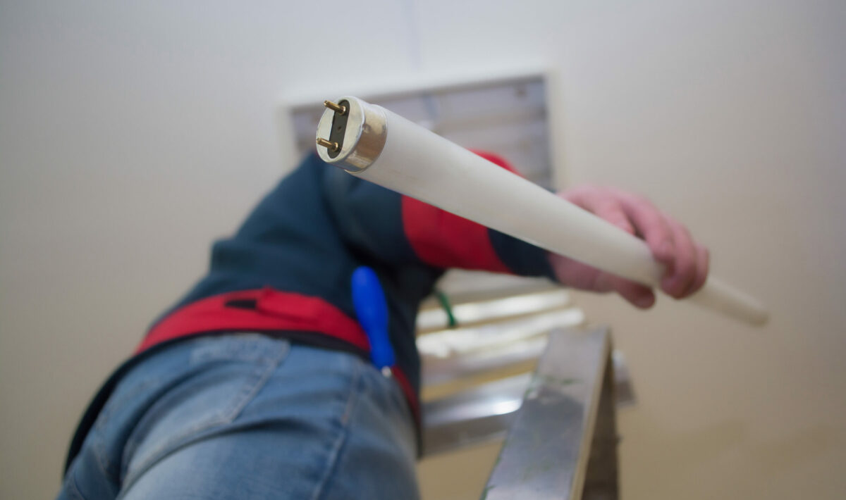 Electrician man worker in uniform installing ceiling fluorescent lamp